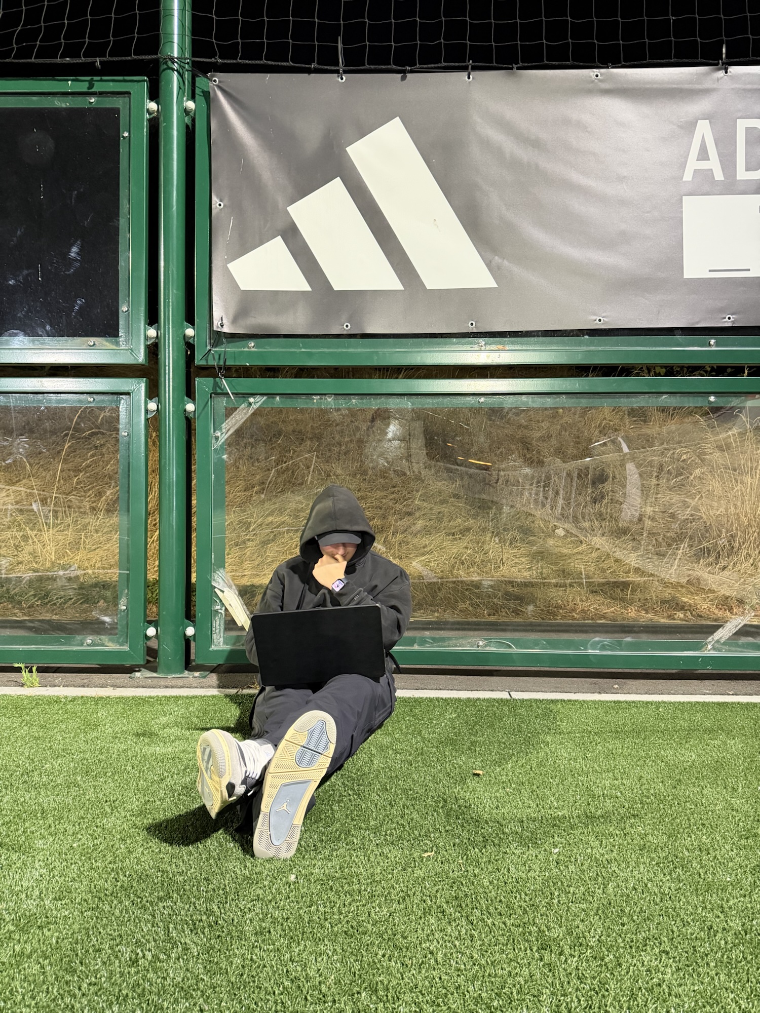 Travail sur ordinateur portable au bord d’un terrain, devant une bâche adidas