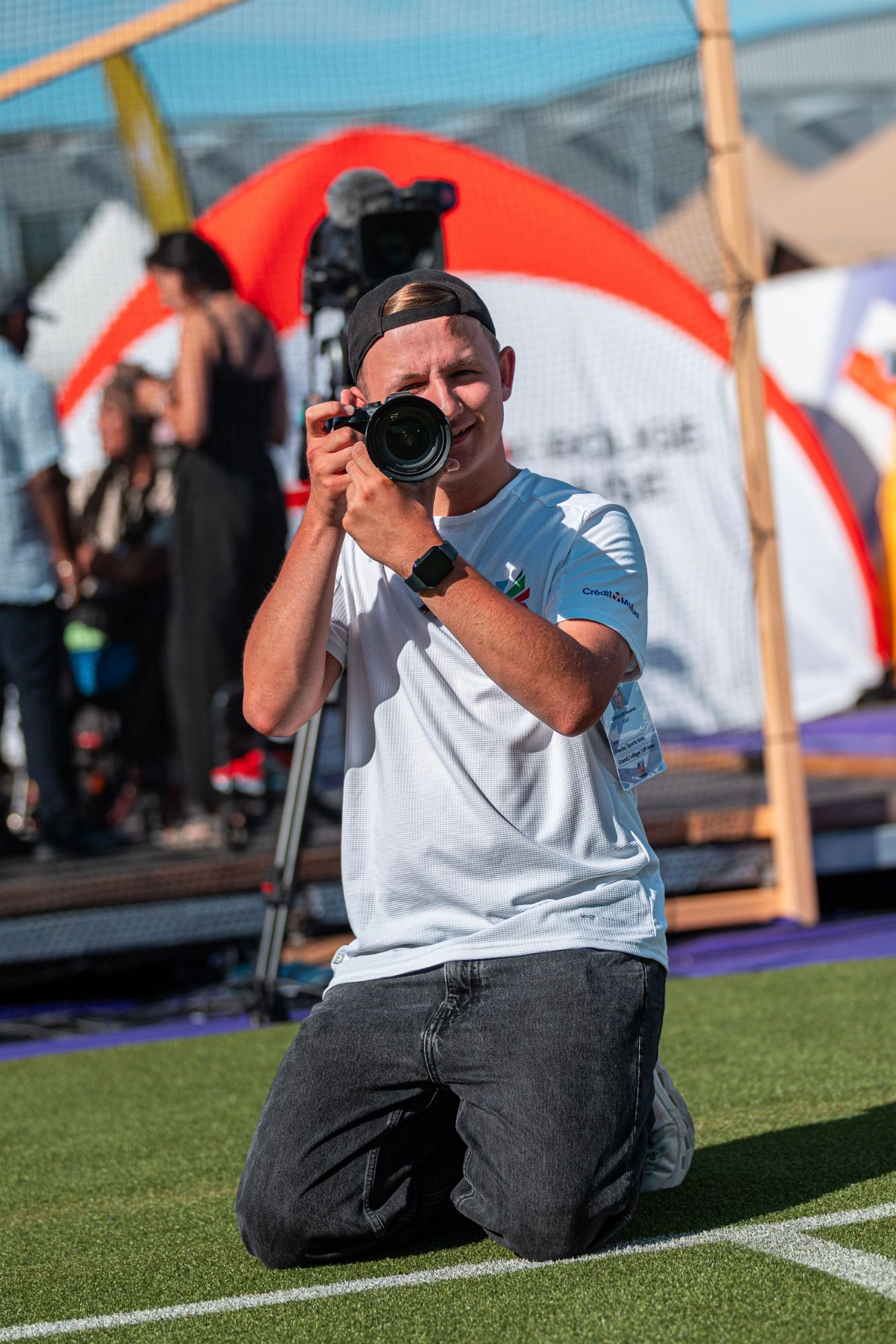 Photographe à genoux sur un terrain, appareil photo au visage, pendant un événement